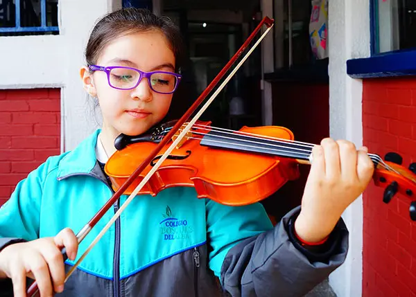 Niña con uniforme escolar interpretando música en violín dentro de un centro educativo en Cuautitlán Izcalli
